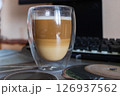Layered Latte Macchiato in a Double-Walled Glass on a Desk 126937562