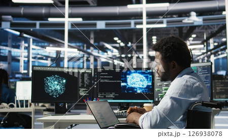Data center computer scientist in wheelchair using AI node tree software to minimize system downtime. Server hub employee in disability using artificial intelligence visual programming tool, camera A Data center computer scientist in wheelchair using AI node tree software to minimize system downtime. Server hub employee in disability using artificial intelligence visual programming tool, camera A 126938078