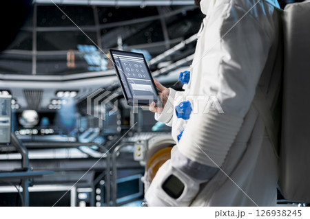 Close up of astronaut using tablet to view spacecraft analytics during scientific mission. Spaceship crew member in spacesuit looking at orbital navigation data on device during planetary exploration Close up of astronaut using tablet to view spacecraft analytics during scientific mission. Spaceship crew member in spacesuit looking at orbital navigation data on device during planetary exploration 126938245