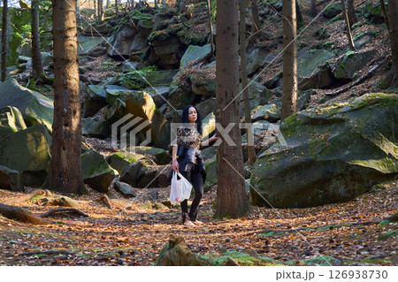 Tired young woman tourist stands near tree among boulders on hike 126938730