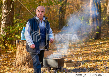 Elderly man pensioner makes a fire for grilling at a picnic in autumn 126938760
