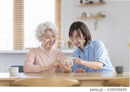 スマートフォンを持ったシニア女性と介護スタッフ スマートフォンを持ったシニア女性と介護スタッフ 126938840