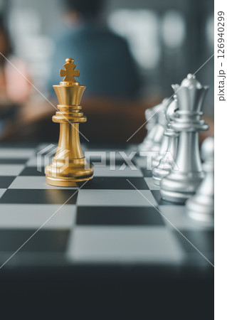 Close-up of a golden king chess piece surrounded by silver pieces on a checkered board, symbolizing strategy and competition. 126940299