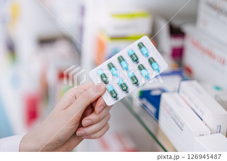Close up Doctor Pharmacist hand holding medicine capsule pills pack with drugs shelf in drug store 126945487