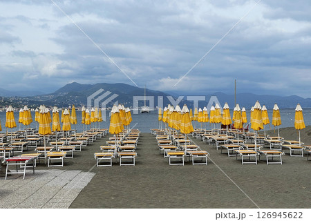 Yellow beach umbrellas and sunbeds near sea against blue sky. Summer and vacation in Liguria, Italy. Background for text. Yellow beach umbrellas and sunbeds near sea against blue sky. Summer and vacation in Liguria, Italy. Background for text. 126945622