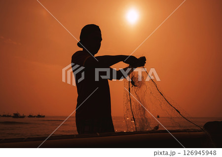 Silhouette of a Vietnamese male fisherman taking out a catch of fish from fishing net in boat on beach by the sea in fishing village at sunset in Vietnam 126945948