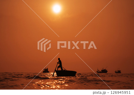 Silhouette of a Vietnamese male fisherman on a round basket boat in the sea in a fishing village in morning at sunrise in Vietnam 126945951