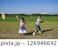 牧草地で麦わら帽子を飛ばして遊ぶ兄妹 126946692