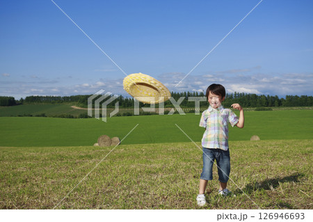 牧草地で麦わら帽子を飛ばして遊ぶ少年 126946693