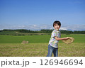 牧草地で麦わら帽子を飛ばして遊ぶ少年 126946694
