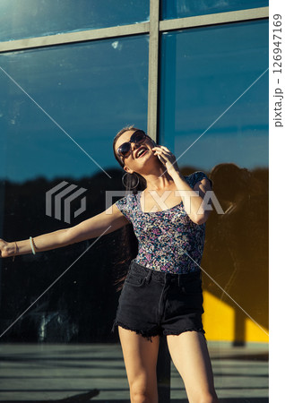 A young woman wearing shorts and a T-shirt stands near the transparent facade, holding a cell phone 126947169