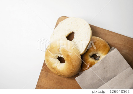 Closeup view of slice of bagel breads from brown paper bag on wooden board isolated over white background. Top view 126948562