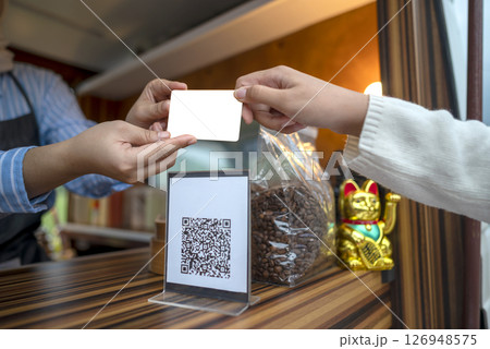Woman gives debit card to female barista for payment after ordering with qr code for payment on the counter table. Mockup or copy space. Small business of a coffee shop or cafe on a truck 126948575