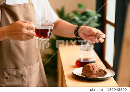 Close up of man in an apron holding a glass cup of black coffee and a piece of bread 126948890