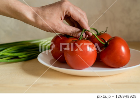 Close-up of a man's hand holding tomatoes by their green tails 126948929