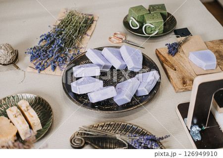 Lavender and green soaps arranged on a table with dried flowers and cutting tools. Aromatherapeutic soap, lavender benefits, functional wellness, plant-based fragrance 126949910
