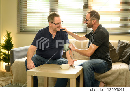 Adult son checking elderly father's blood pressure at home. Health care concept Adult son checking elderly father's blood pressure at home. Health care concept 126950414