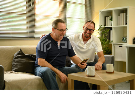 Senior man and his grown son laughing while browsing on a mobile phone in living room. Father day concept 126950431