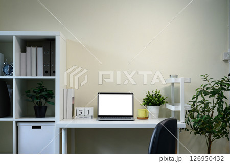 Organized home office workspace with blank screen laptop, indoor plants, and minimalist calendar 126950432