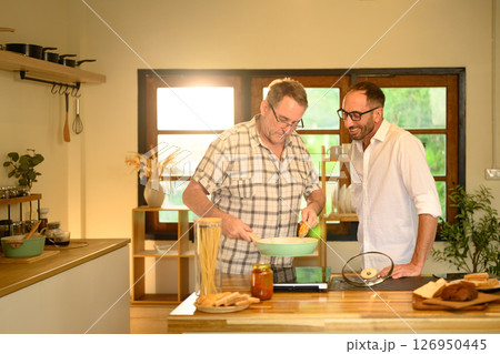 Smiling father and adult son preparing a pasta meal together in a cozy home kitchen. Father day concept 126950445