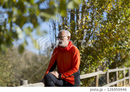 Senior man in bright orange hoodie resting on wooden fence Senior man in bright orange hoodie resting on wooden fence 126950946