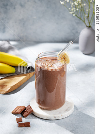 Chocolate smoothie with banana in a glass on a  blue background with fresh fruits and sunlight. 126951087