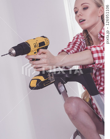 Woman using drill on ladder Woman using drill on ladder 126951106