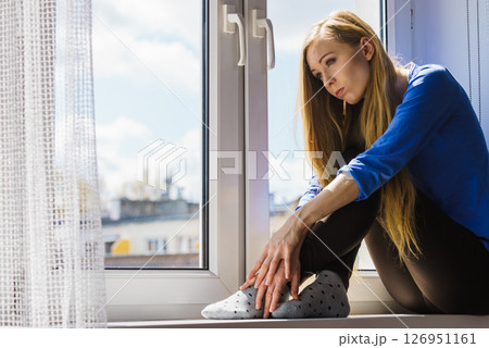 Sad depressed teen girl sitting on window sill Sad depressed teen girl sitting on window sill 126951161