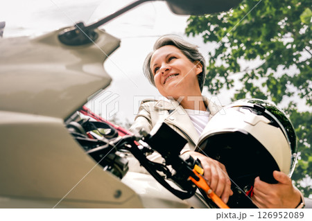 Confident gray-haired woman holding helmet beside motorcycle, symbol of freedom and graceful aging Confident gray-haired woman holding helmet beside motorcycle, symbol of freedom and graceful aging 126952089