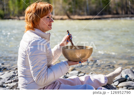 Woman performing a sound ritual with a Tibetan singing bowl by the Altai river. Concept of feminine energy, sacred vibration, and shamanic connection to the Earth Woman performing a sound ritual with a Tibetan singing bowl by the Altai river. Concept of feminine energy, sacred vibration, and shamanic connection to the Earth 126952790