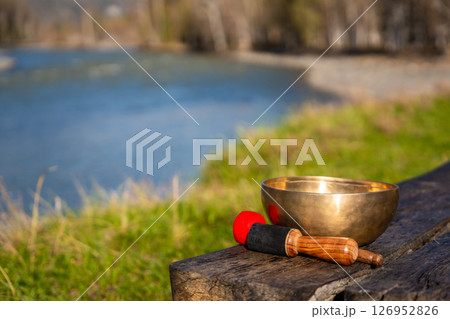 Tibetan singing bowl resting on a wooden bench by the Altai river. Concept of sacred stillness, energy resonance, and spiritual presence in untouched nature. Tibetan singing bowl resting on a wooden bench by the Altai river. Concept of sacred stillness, energy resonance, and spiritual presence in untouched nature. 126952826