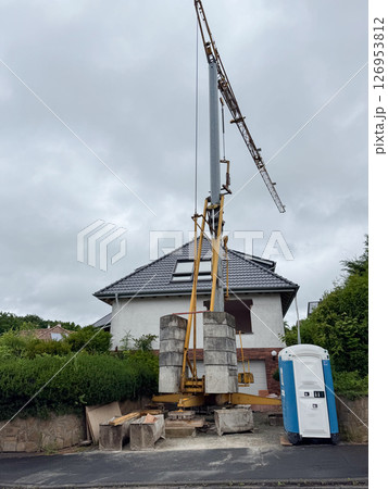 Large construction crane setup near a residential house with a portable restroom nearby. The scene highlights urban development work and infrastructure changes in progress. 126953812