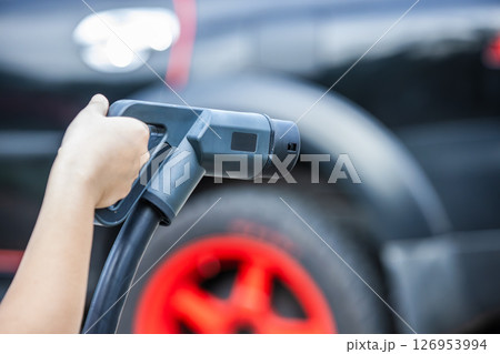 Closeup hand holding electric car charger head plug for charging EV car at ev charger station Closeup hand holding electric car charger head plug for charging EV car at ev charger station 126953994