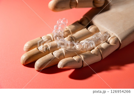 Close-up of wooden elegant hand holding invisible clear aligners, on pastel pink background. Healthy lifestyle and teeth concept 126954266
