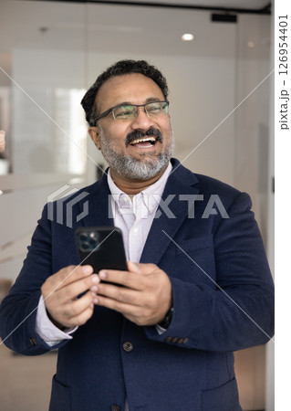 Happy Indian businessman in suit standing in workplace with smartphone 126954401