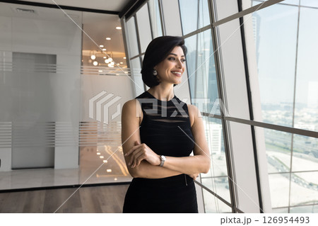 Confident Armenian businesswoman dressed in dress looks out panoramic window Confident Armenian businesswoman dressed in dress looks out panoramic window 126954493