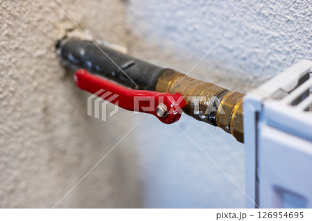 Here is a detailed closeup view of a red valve located on a pipe 126954695