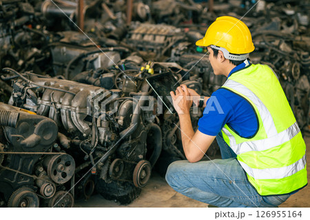 technician male worker working in scrapyard finding used car engine block order from customer at storage recycle area in warehouse 126955164