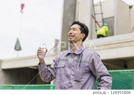 Asian worker male thirsty drinking water in hot summer weather working outdoor at construction site Asian worker male thirsty drinking water in hot summer weather working outdoor at construction site 126955806