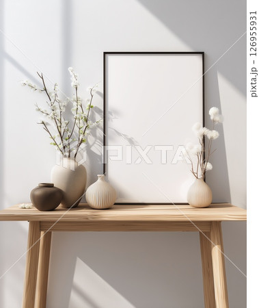 A minimalist white frame sits on a wooden table, accented by elegant vases and blooms 126955931