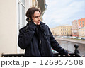 A young man wears a black coat and speaks on the phone or smartphone 126957508