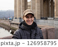 Young man smiles while standing on a bridge in a city with historic architecture during a cool day. waist up portrait 126958795