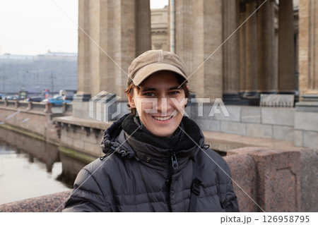 Young man smiles while standing on a bridge in a city with historic architecture during a cool day. waist up portrait 126958795