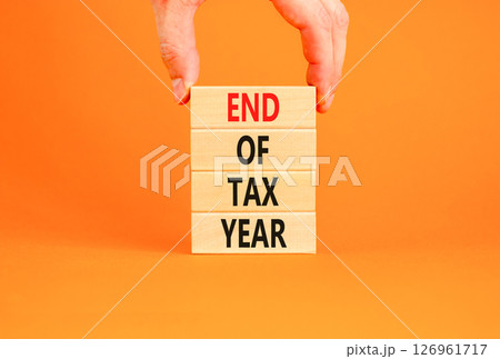 End of tax year symbol. Concept words phrase End of tax year on beautiful wooden blocks. Beautiful orange paper background. Businessman's hand. Business End of tax year concept. Copy space. 126961717
