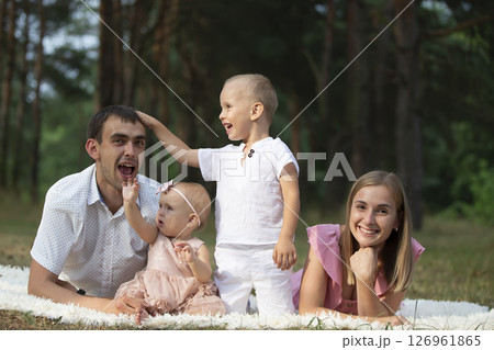 Husband and wife and their little children. Family portrait in nature. Mom and Dad with their brother and sister are lying on the grass. Young family with children for a walk. 126961865