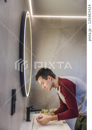 Young man washes his hands under running water in a modern bathroom, calmly following a healthy hygiene routine. Young man washes his hands under running water in a modern bathroom, calmly following a healthy hygiene routine. 126963424