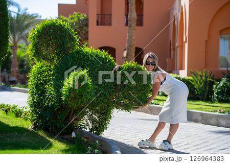 A woman stands in front of a bush that looks like an elephant 126964383