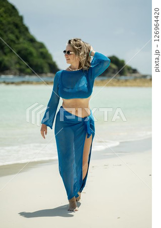 Beautiful girl in blue beach dress walking along wild beach on island Beautiful girl in blue beach dress walking along wild beach on island 126964420