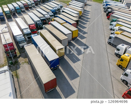 Aerial view of a large truck parking lot at a logistics hub, with multiple commercial semi trucks parked in organized rows. 126964696