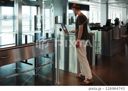 A young man uses her smartphone to scan a boarding pass at an automated airport gate. Concept of digitalization, self-check-in and independent travel. 126964743
